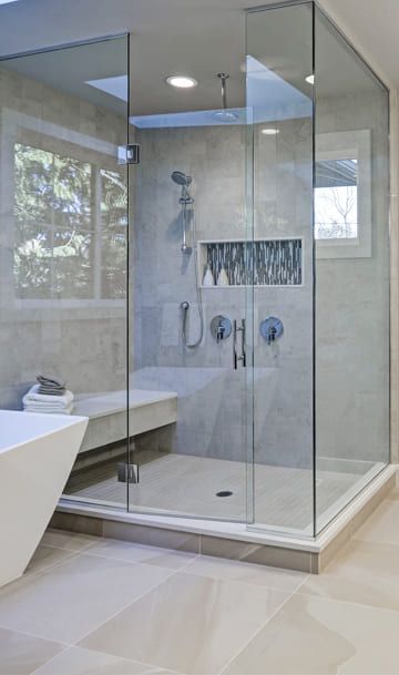 Modernes Badezimmer mit Glasduschabtrennung, eleganten Armaturen, eingebauter Sitzbank und freistehender Wanne. Helle und luftige Atmosphäre.
