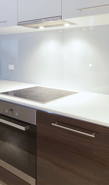 Moderne Küche mit eleganten Schränken, einem Induktionskochfeld und Unterbauleuchten auf einer sauberen, weißen Arbeitsplatte.