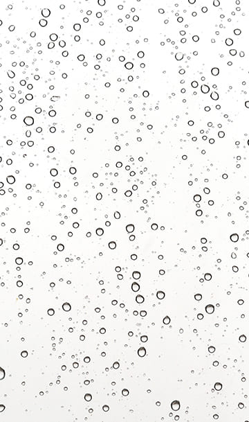 Nahaufnahme zahlreicher klarer Wassertröpfchen auf einer glatten, weißen Oberfläche, die ein Muster unterschiedlicher Größe und Form bilden.