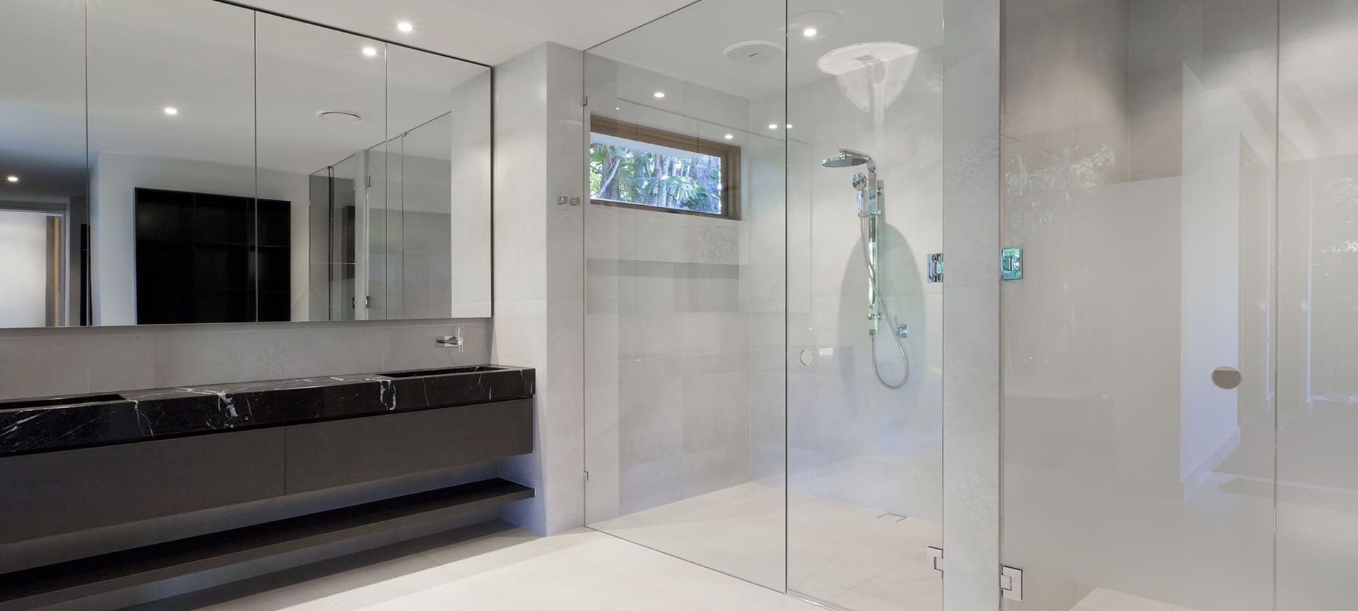 Ein modernes Badezimmer mit einem eleganten schwarzen Waschtisch, einer Glasduschkabine und großen Spiegeln, die ein helles und luftiges Design präsentieren.